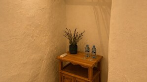 Une pièce d’angle avec un meuble en bois, un portant à vêtements, une plante en pot et deux bouteilles d’eau sur une petite table.