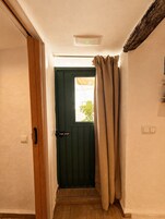 Un pasillo estrecho con una puerta de madera, una ventana con cortina y un interruptor de luz en la pared.