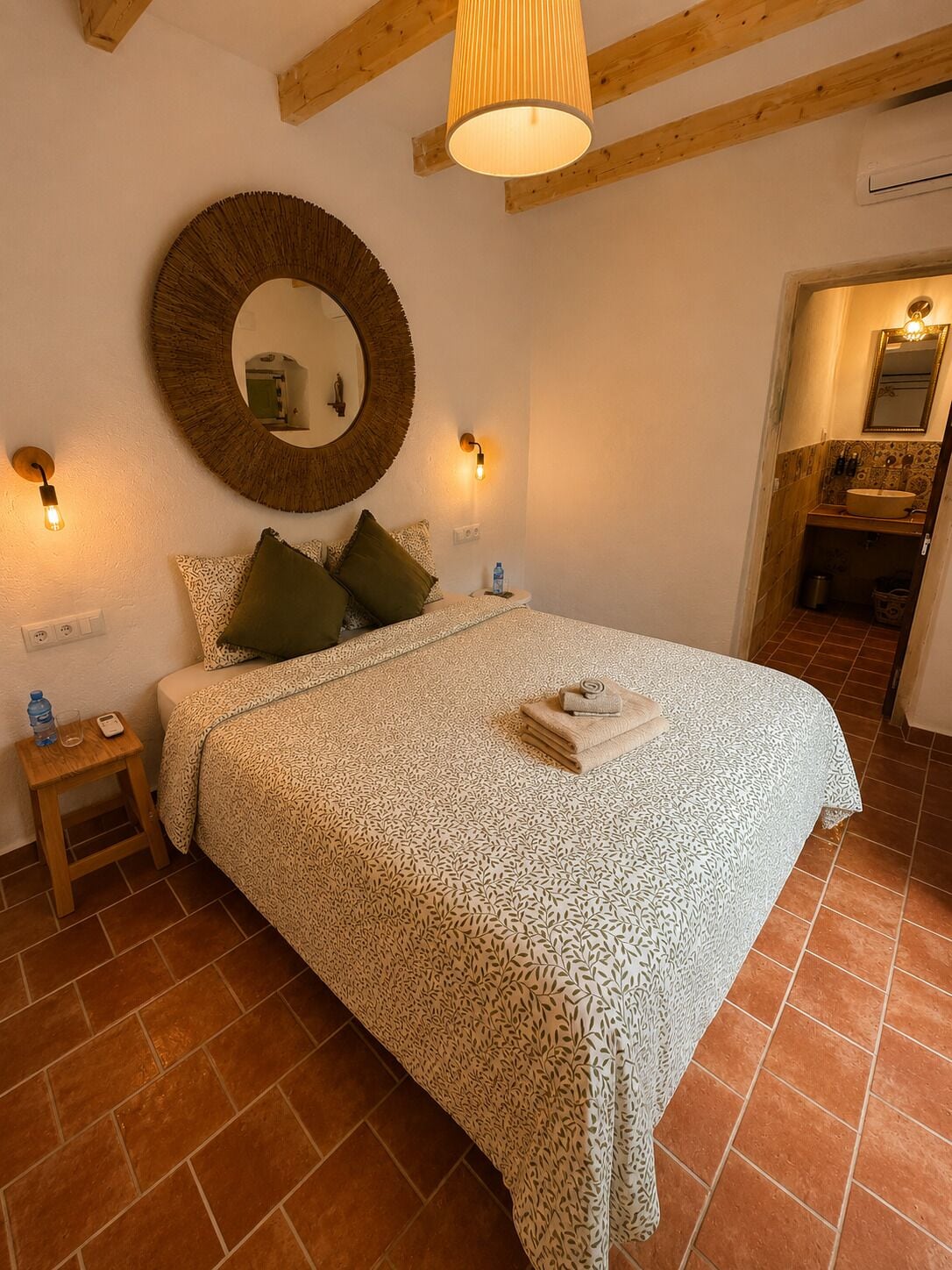 Un dormitorio con cama, un espejo redondo, lámparas de noche y una mesita de noche pequeña.