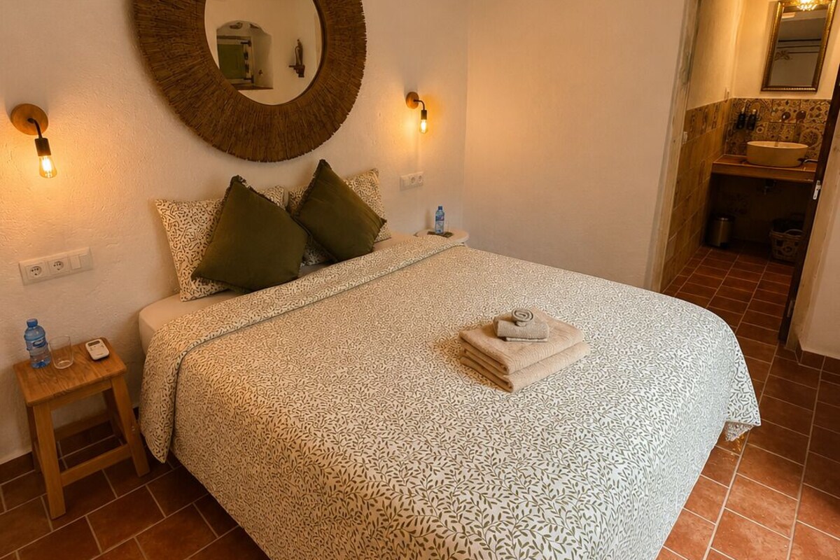 Un dormitorio con cama, un espejo redondo, lámparas de noche y una mesita de noche pequeña.