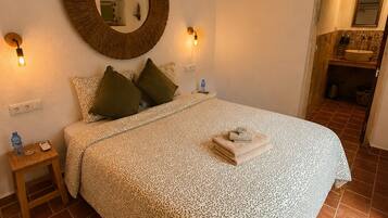 Un dormitorio con cama, un espejo redondo, lámparas de noche y una mesita de noche pequeña.