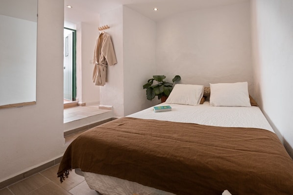Un dormitorio con una cama grande, una mesita de noche, una ventana y una planta.