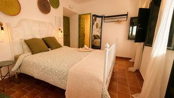 Un dormitorio con cama, mesita de noche, lámpara colgante, espejo y puerta.