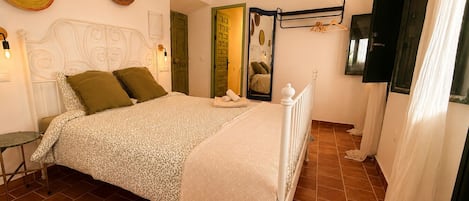 A bedroom with a bed, a bedside table, a hanging light fixture, a mirror, and a door.