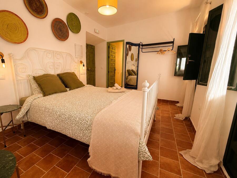 Un dormitorio con cama, mesita de noche, lámpara colgante, espejo y puerta.