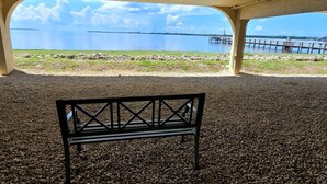 A bench under a covered area with a view of a calm lake and a pier. - Beach Retreat w/ Pool & Fishing Dock (Port Charlotte)