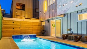 Ein Schwimmbecken mit Wasserfall, Holzterrasse und Sitzbereich im Freien.