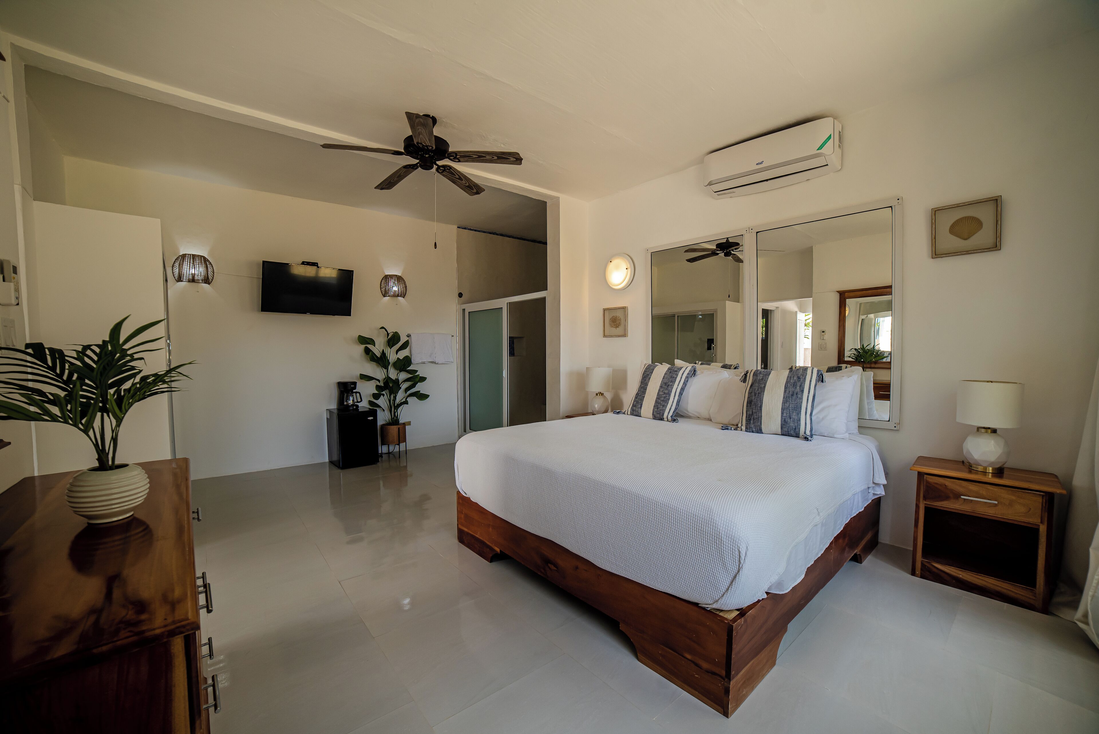 A spacious bedroom with a large bed, ceiling fan, air conditioning unit, and a bedside table with a lamp.