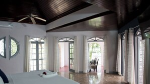 A spacious room with a large bed, a ceiling fan, and multiple windows with curtains.