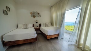 A hotel room with two beds, a nightstand, a wall clock, and a view of the sea.