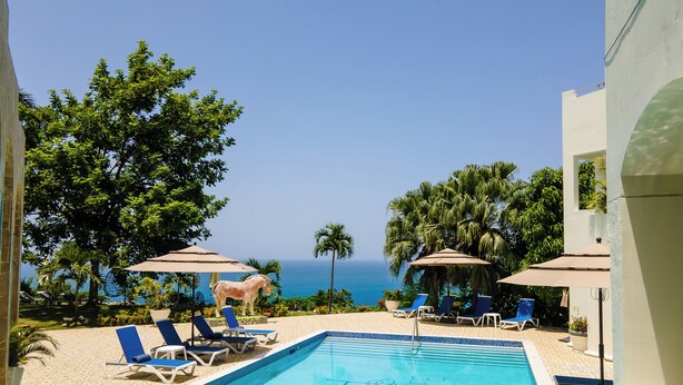 A pool area with lounge chairs and umbrellas, a decorative horse statue, and a view of the ocean.