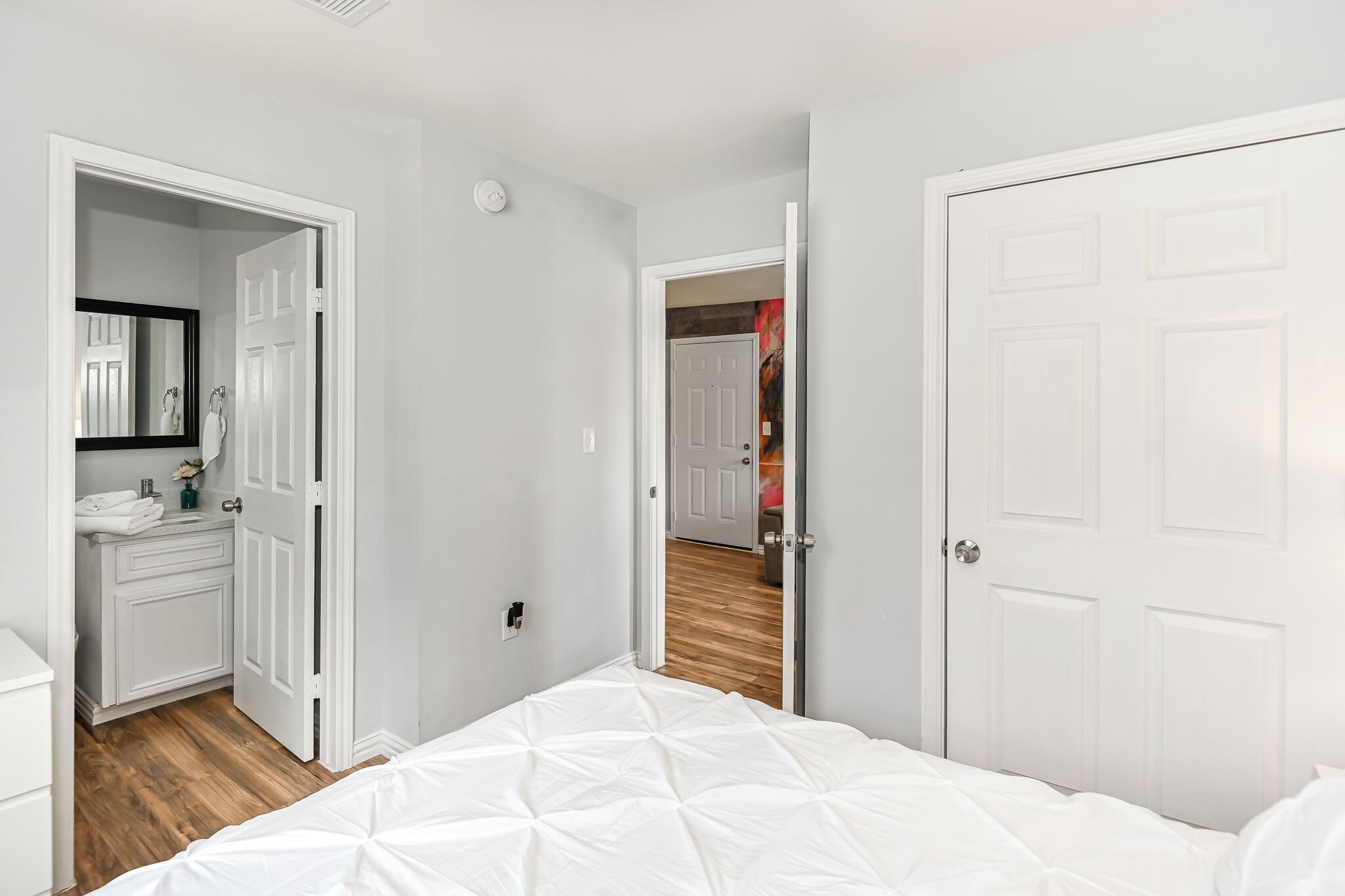 A bedroom with a white bed, a white wardrobe, and a bathroom with a mirror and sink.