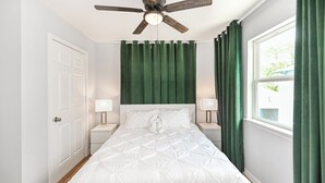 A bedroom with a bed, two bedside tables with lamps, a ceiling fan, a window with curtains, and a door.