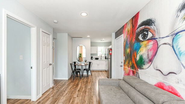 A modern living room with a gray sofa, wooden flooring, and a colorful abstract painting on the wall.