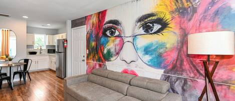 Ein modernes Wohnzimmer mit grauem Sofa, einem Essbereich mit Tisch und Stühlen sowie einer Küche im Hintergrund.