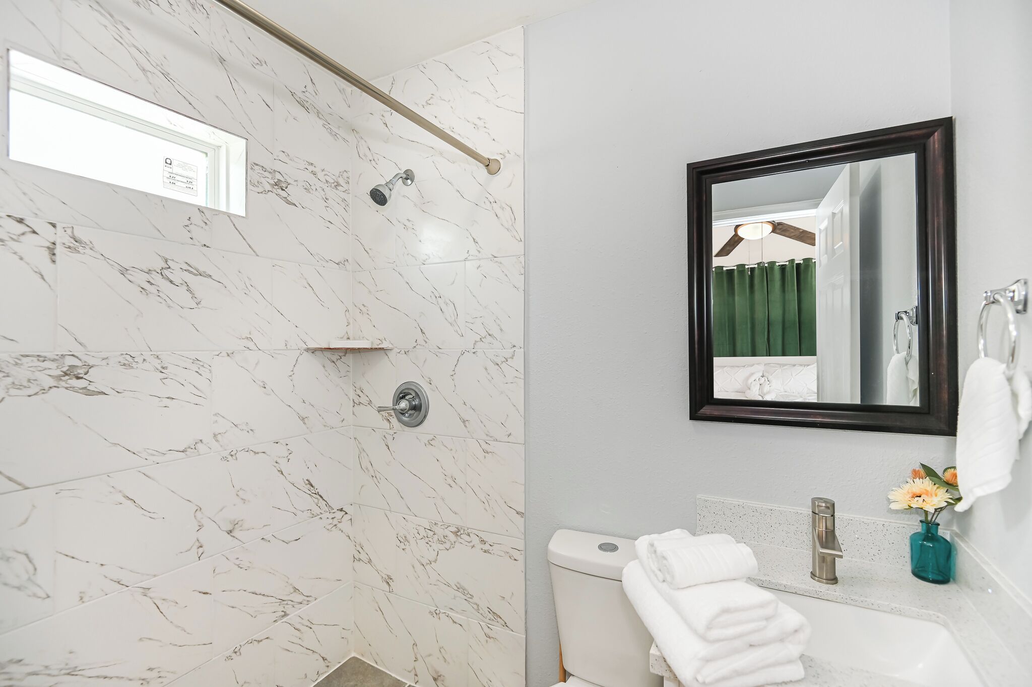 Een badkamer met een douchewand van marmer, een toilet, een wastafel met spiegel en een handdoekhouder.
