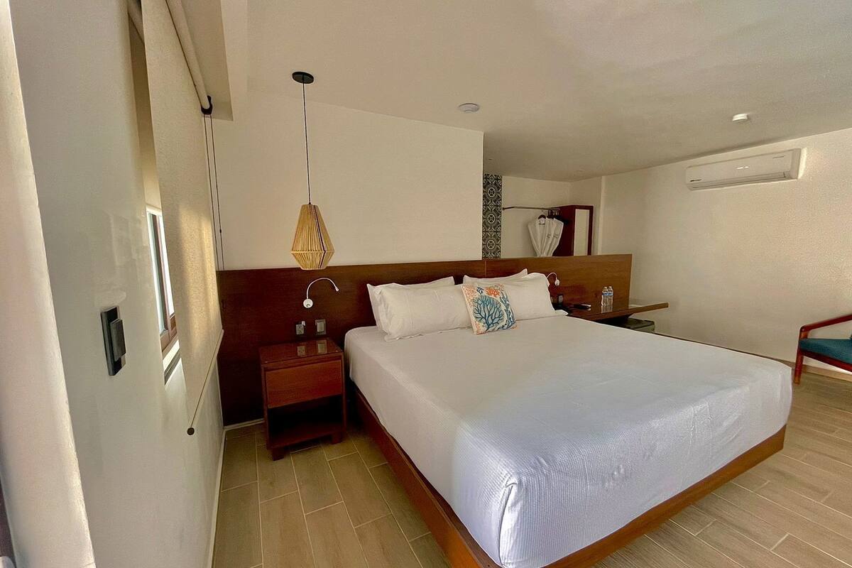 A hotel room with a large bed, wooden headboard, bedside tables, a hanging lamp, and a mirror on the wall.