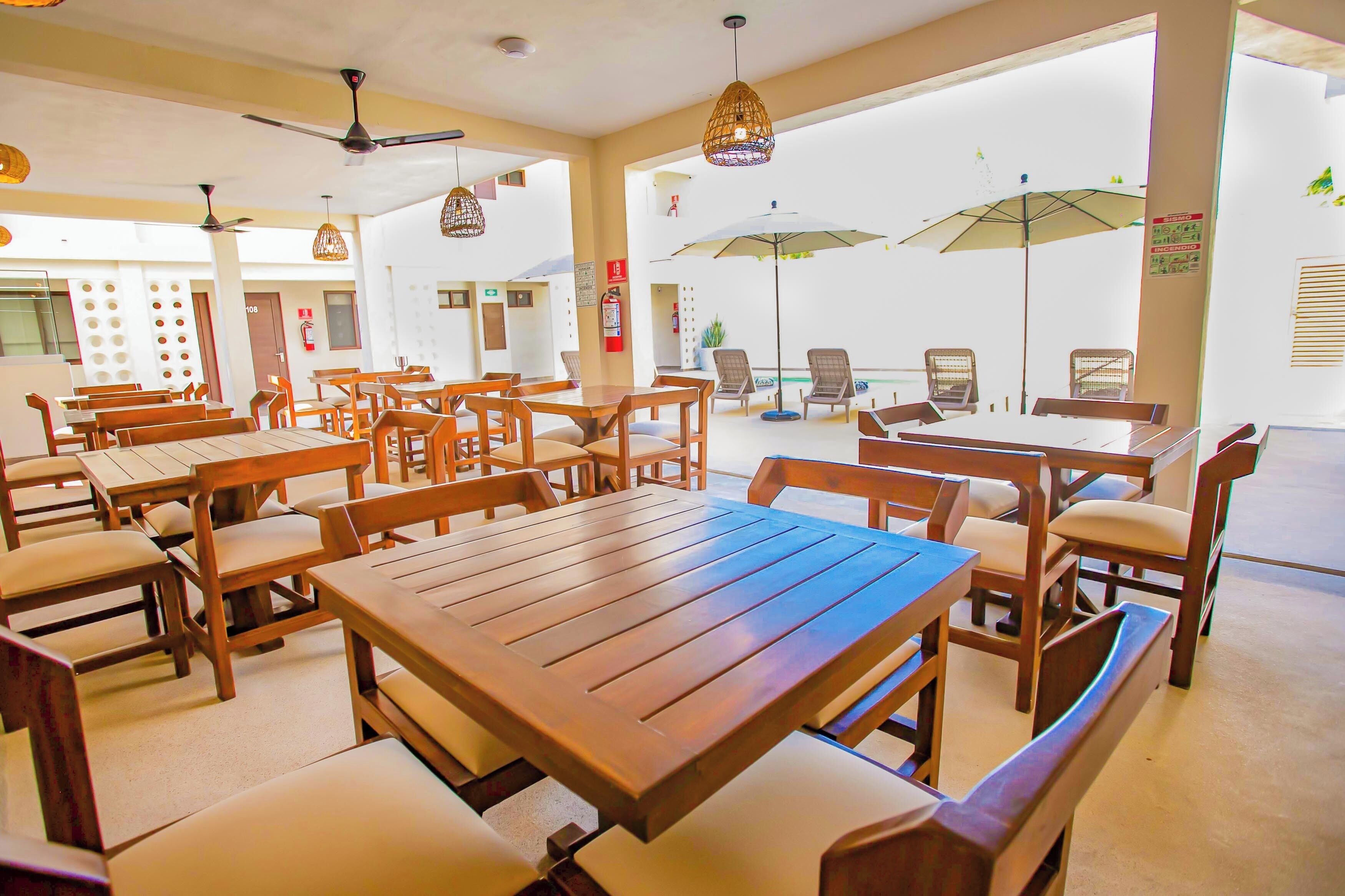 A spacious indoor dining area with multiple wooden tables and chairs, ceiling fans, and hanging pendant lights.