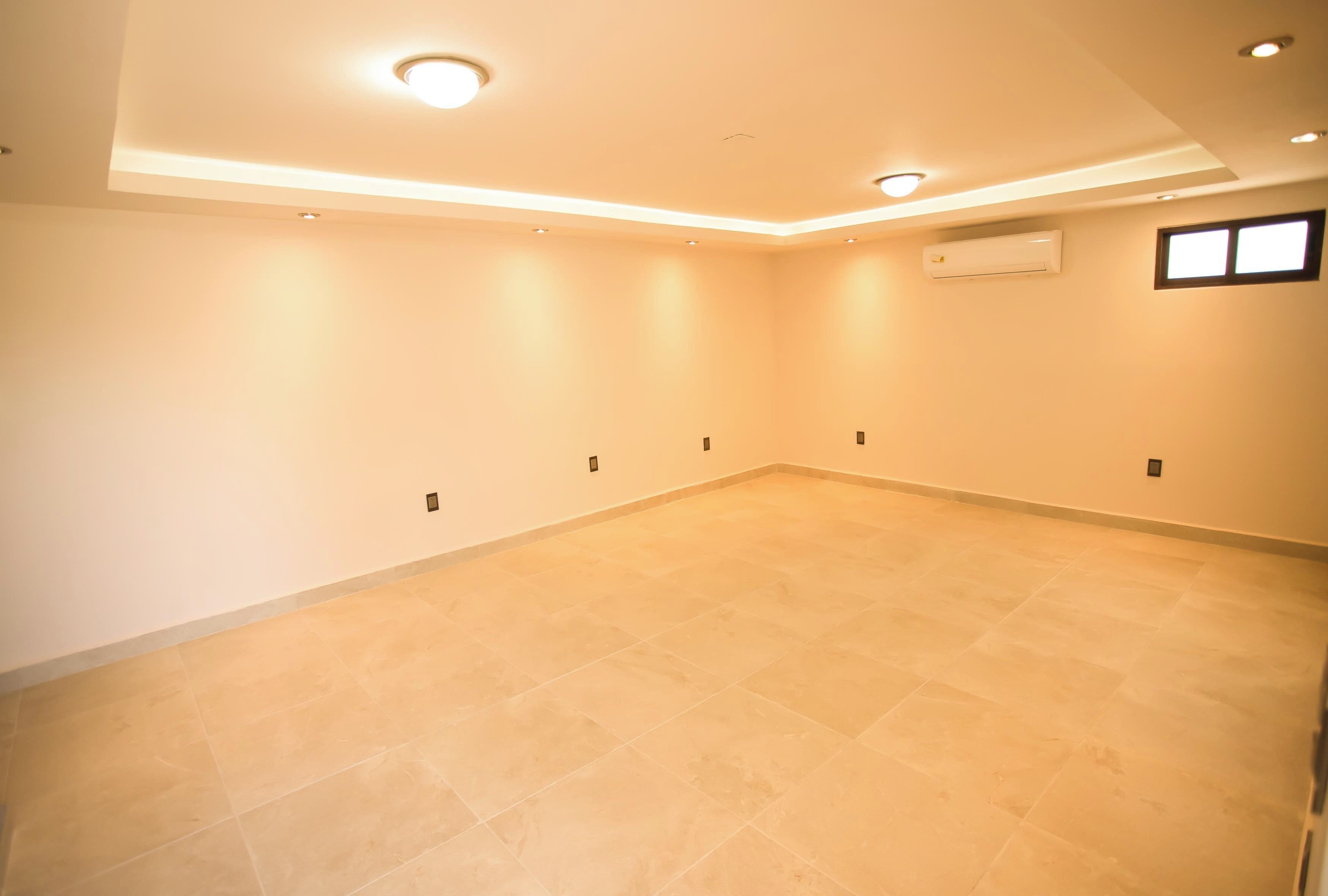 Une pièce spacieuse avec un sol carrelé de couleur beige, des spots encastrés au plafond et un appareil de climatisation fixé au mur.