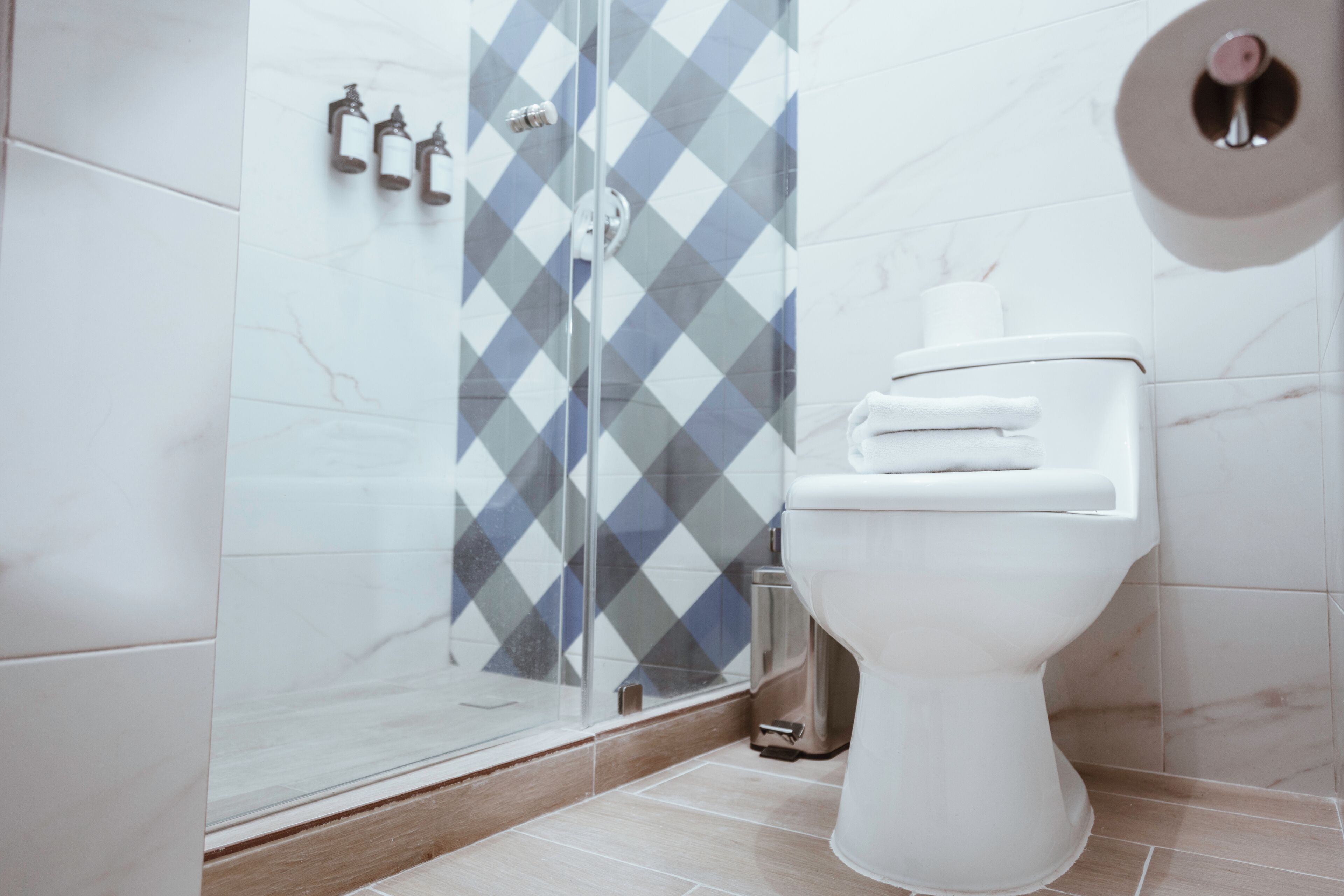 Un baño moderno con cabina de ducha de vidrio, inodoro blanco y pared con diseño de mármol.