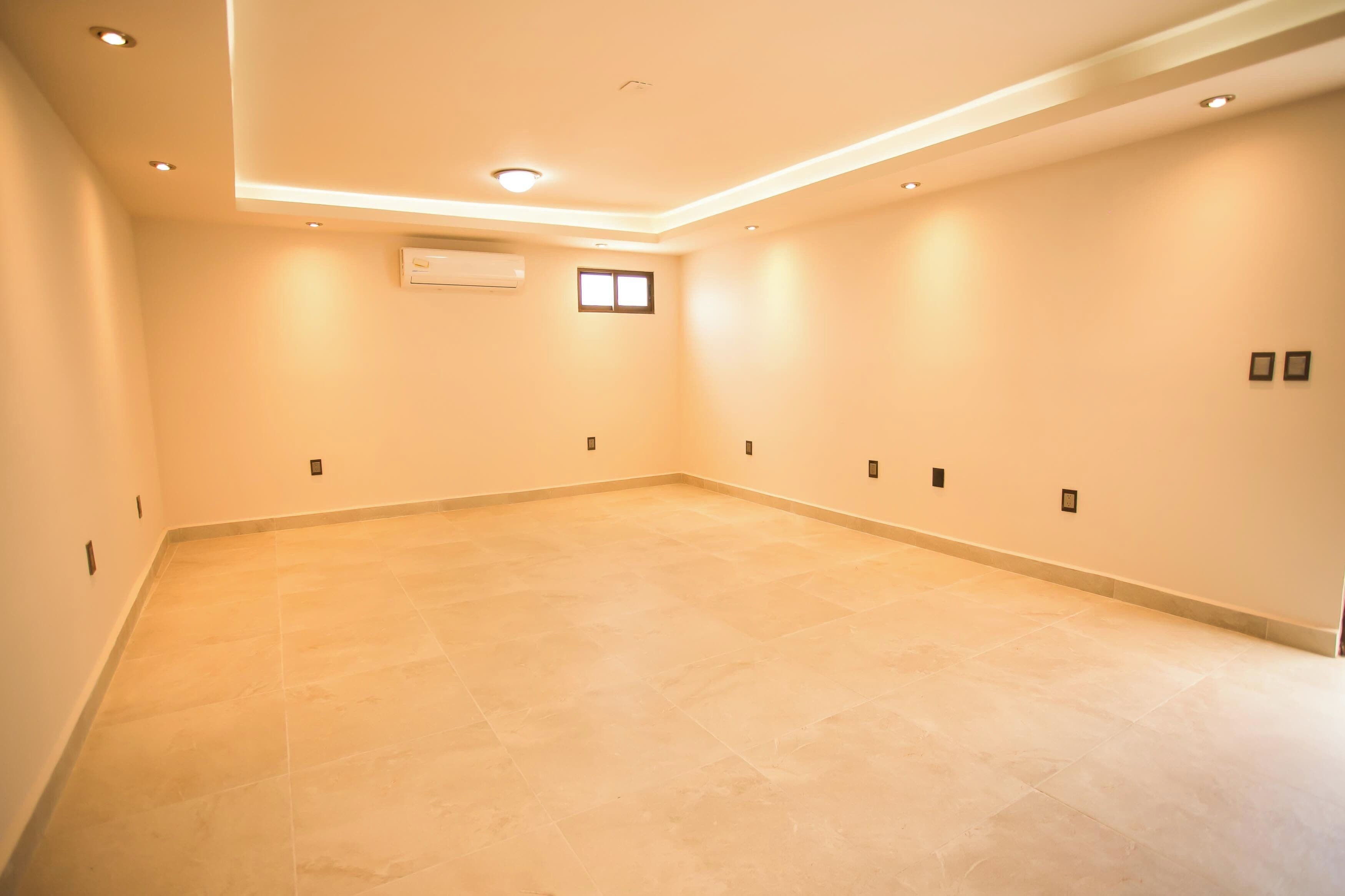A spacious room with a tiled floor, recessed ceiling lights, and a small window.