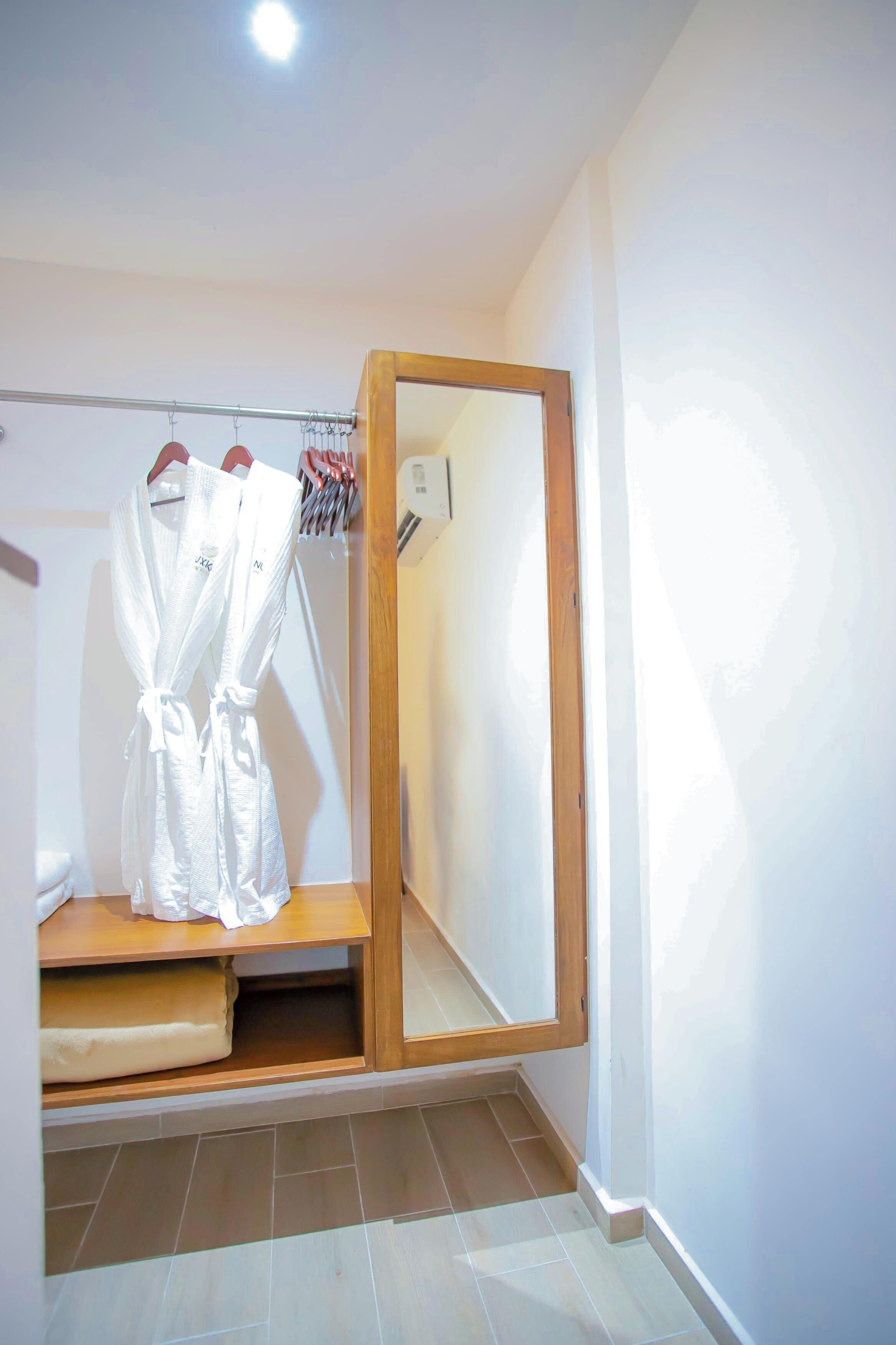 Un baño con tocador de madera, espejo y perchero con batas blancas.