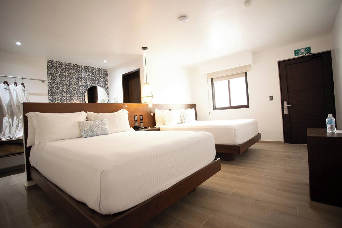 A hotel room with two beds, a wooden headboard, a bedside table with a lamp, a wardrobe, and a patterned wall.