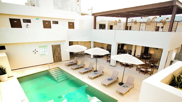 A rooftop pool area with lounge chairs and umbrellas, a staircase leading to upper floors, and a dining area with tables and chairs. - Hotel Yuhome Telchac (Telchac Puerto)