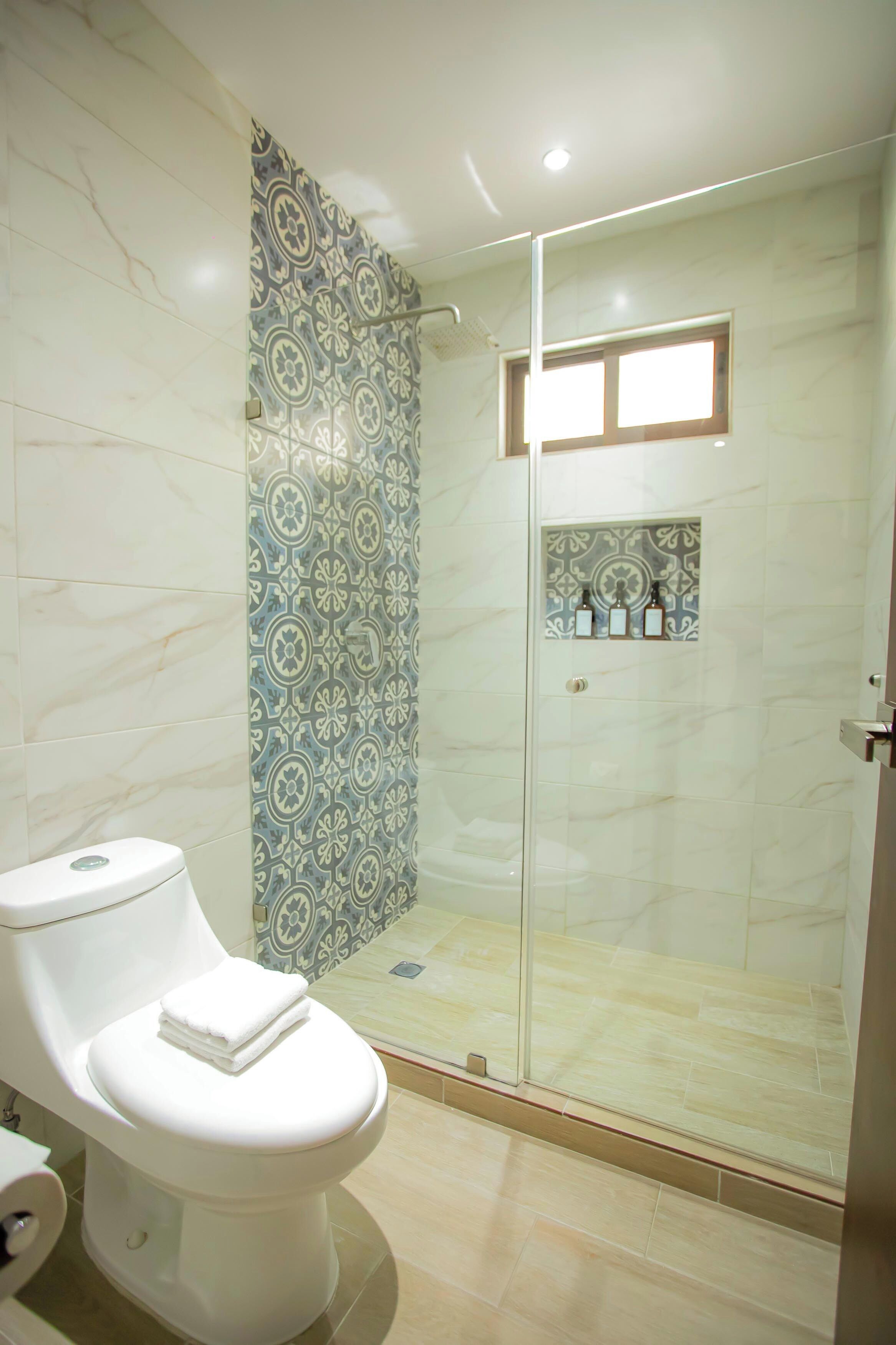 Un baño moderno con inodoro, ducha y cabina de ducha con mampara de vidrio.