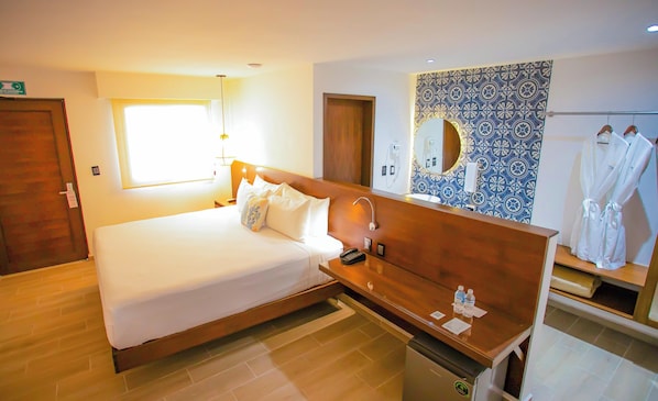 A hotel room with a bed, bedside table, a mirror, a small desk with a phone, and a bathroom with a towel rack. - Hotel Yuhome Telchac (Telchac Puerto)