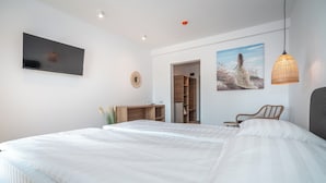 A modern bedroom with a large bed, a TV mounted on the wall, a wooden wardrobe, and a painting of a woman in a field. - Spot Vama Veche (Limanu)