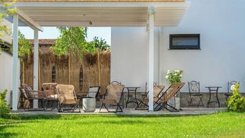 Un patio al aire libre con pérgola, mobiliario de mimbre y un muro de piedra.