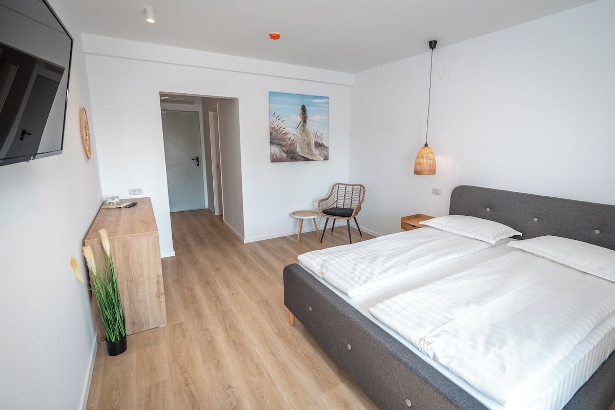 A modern bedroom with a large bed, a small desk, a chair, and a television mounted on the wall.