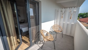 A balcony with two wicker chairs and a small table, a sliding glass door leading to a bedroom, and a white picket fence. - Spot Vama Veche (Limanu)
