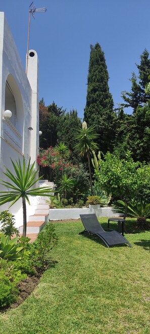 Un jardin avec un bâtiment blanc, un fauteuil de relaxation noir et un grand arbre.