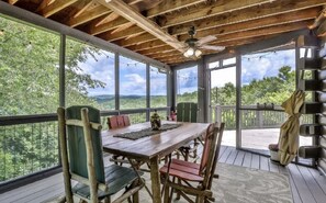A wooden deck with a table and chairs, large windows, and a view of the outdoors. - Gorgeous Lake View Log Cabin with Hot Tub! (Ellijay)