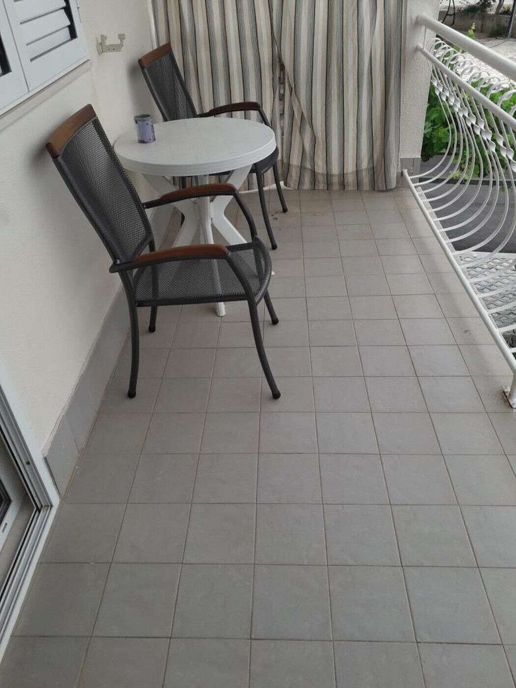 Ein Balkon mit rundem Tisch, zwei Stühlen, einem gestreiften Vorhang und einem weißen Geländer.