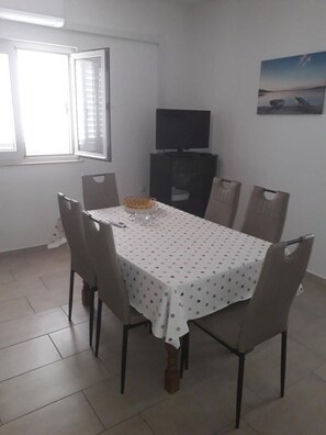 Un coin repas avec une table recouverte d’une nappe blanche à pois, entourée de six chaises.