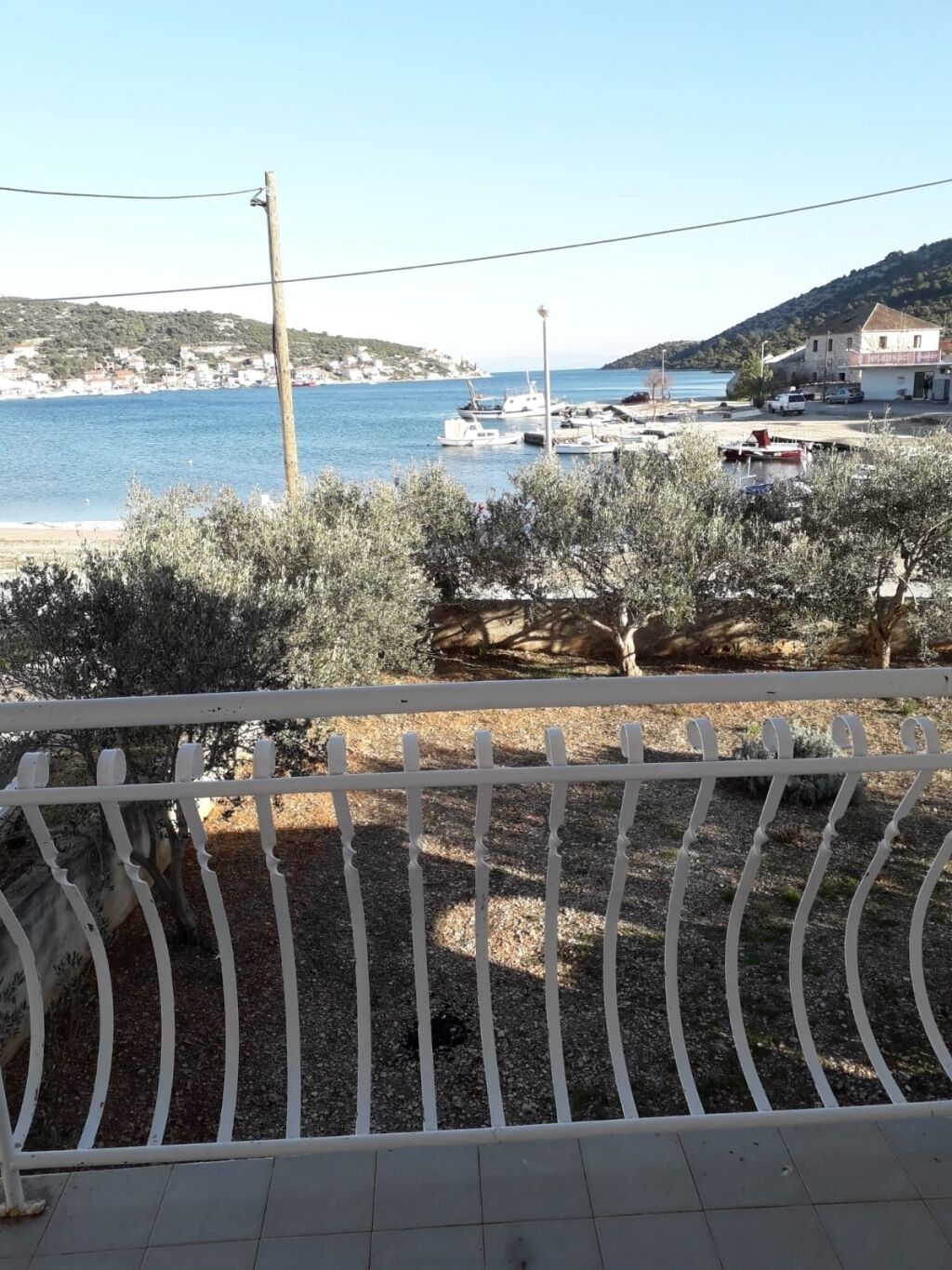 A coastal view with a marina, olive trees, and a white fence.