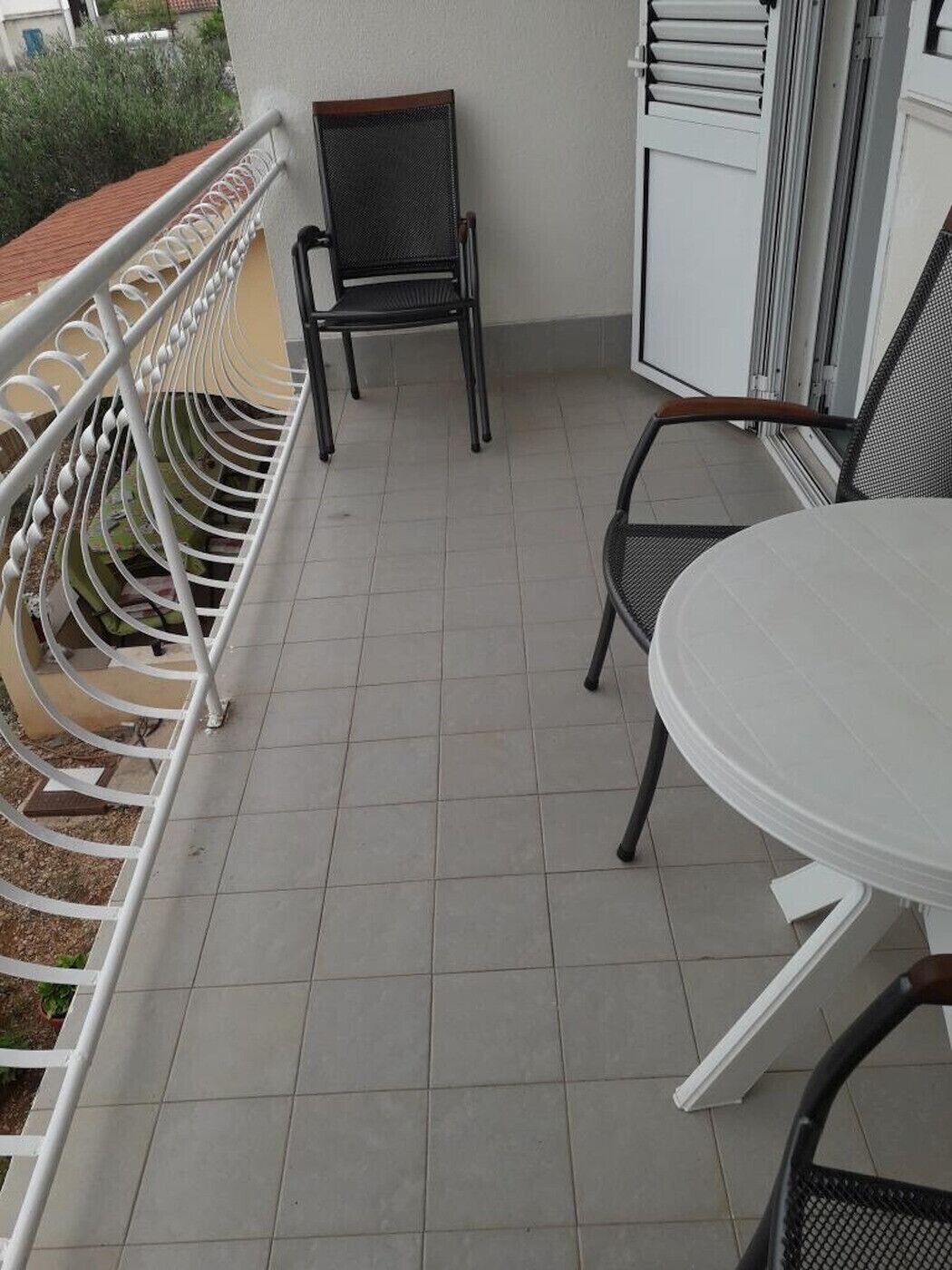 A balcony with a white table and two chairs, a metal railing, and a door with a window.