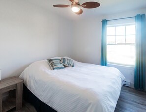 A bedroom with a bed, a nightstand, a ceiling fan, and a window with curtains.