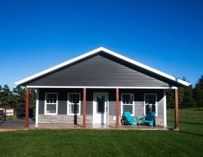 A single-story house with a covered porch, a front door, and two chairs on the porch.