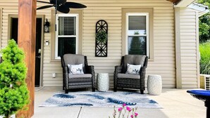 A covered porch with two wicker chairs, a ceiling fan, and a decorative wall piece.