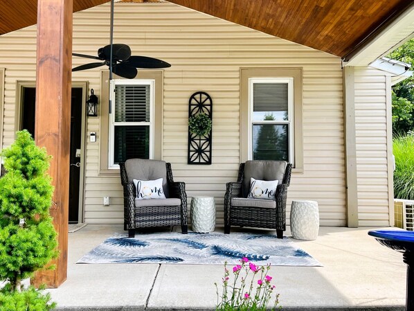 Un portico coperto con due poltrone in vimini, una ventola a soffitto e un elemento decorativo a parete.