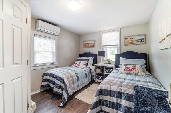 A bedroom with two beds, a white door, an air conditioning unit, and a window with blinds.