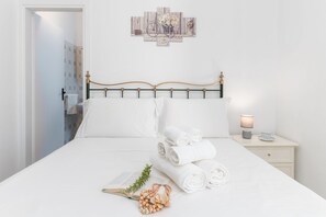Un lit bien fait, avec du linge de lit blanc, une lampe de chevet et une petite table sur laquelle se trouvent une tasse et une soucoupe.