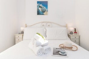 Un lit bien fait, avec des draps blancs, une serviette pliée, un chapeau de paille et un magazine posés sur le lit.