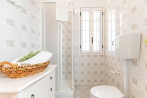 Une salle de bain avec une douche, des toilettes et un panier contenant une serviette, posé sur un comptoir.