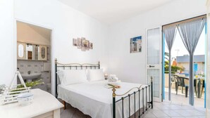 Un dormitorio con cama, mesita de noche, ventana con cortinas y vistas al exterior.