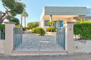 Un bâtiment moderne doté d’une entrée pavée de pierres, d’une allée bordée de grilles et d’une plaque numérotée.